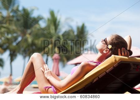 Happy young woman in bikini enjoying her time on chaise-longue luxury pool side