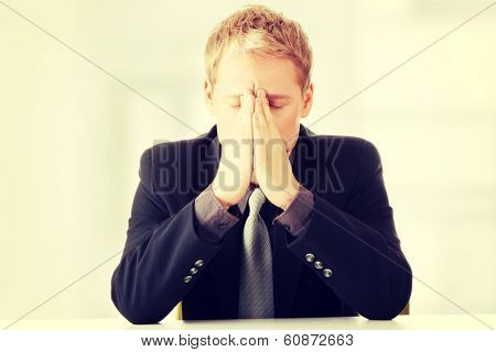 Young businessman sitting behind the desk and being worried