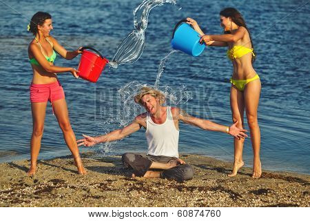 Friends with plastic containers splashing water over one another's heads at the beach 