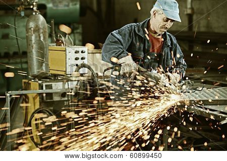 Industrial worker cutting and welding metal with many sharp sparks
