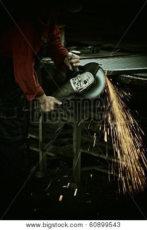 Industrial worker cutting and welding metal with many sharp sparks