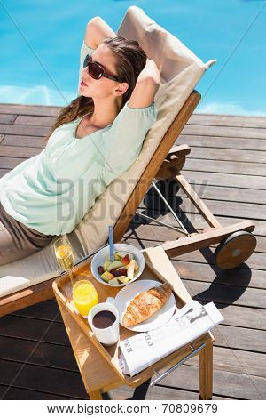 Beautiful young woman relaxing by swimming pool with breakfast on table