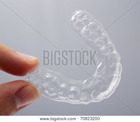 Hand holding a translucent essix retainer