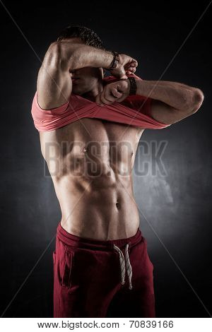 Brutal athletic man taking shirt off on gray background
