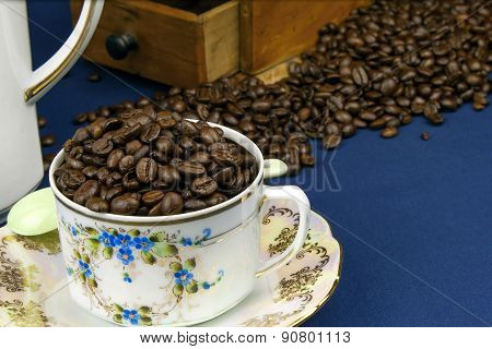 coffee mug on the table with a blue tablecloth, poured out coffee beans