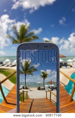 Smatrphone and a landscape. Idea of taking shots, accessing apps, Internet, blogs and others. The blur image is a sunny day at Arraial d'Ajuda Eco Resort in Bahia - Brazil.