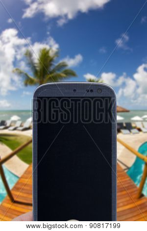 Smatrphone and a landscape. Idea of taking shots, accessing apps, Internet, blogs and others. The blur image is a sunny day at Arraial d'Ajuda Eco Resort in Bahia - Brazil.