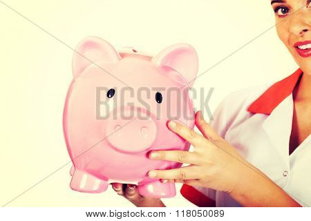 Young beautiful female doctor or nurse holding a piggybank