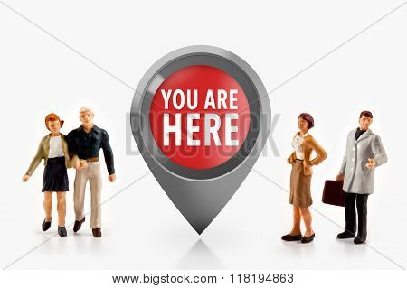 miniature people  - people stand in front the sign you are here