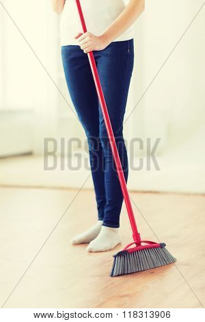 people, housework, cleaning and housekeeping concept - close up of woman legs with broom sweeping floor at home