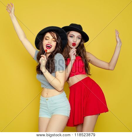 Two young smiling pretty beautiful girls wearing hats holding candies.