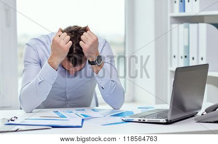 business, people, paperwork and deadline concept - stressed businessman with papers and charts sitting at table in office