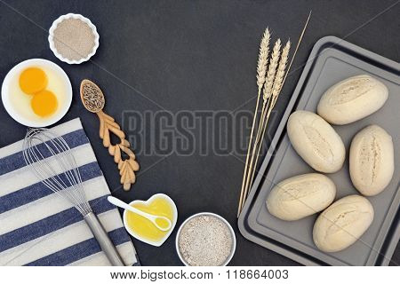 Bread dough rolls and baking ingredients with baking utensils, wheat sheaths and grain in a love spoon on grey slate background.
