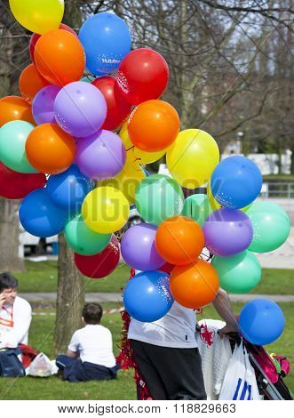 CLACTON ON SEA, ESSEX, ENGLAND, UK- 1 JULY 2015- a man pushing his small baby in a pushchair in the park, and holding multicolored balloons.