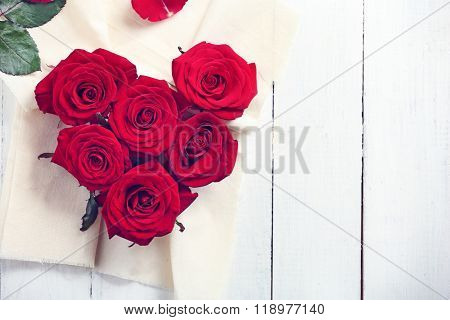 Fresh red roses buds in shape of heart with linen fabric on wooden background