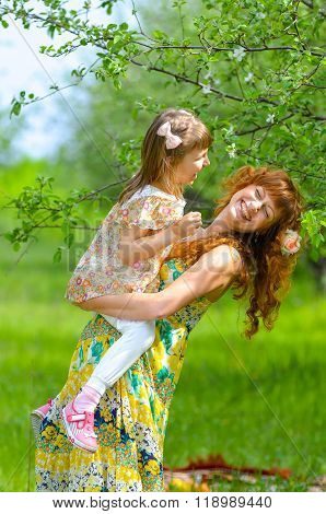 Happy young mother and her daughter walking in the garden in spring