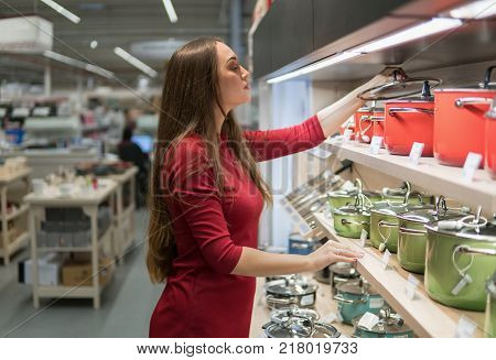 Smart housewife woman buys a saucepan in supermarket. Wide choice of kitchen utensils and cookware