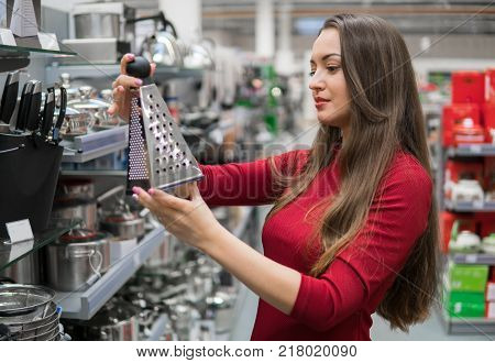 Smart housewife woman buys kitchen grater in supermarket. Wide choice of kitchen utensils and cookware