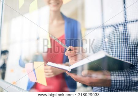 Manager with open notebook and pen pointing at one of reminders on noteboard