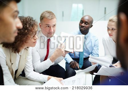 One of intercultural managers pointing at page of notebook with points of his business plan