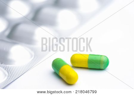 Green and yellow capsules on white background. Two medication pills with foil pack.