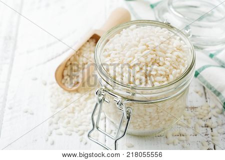 Raw White rice variety Arborio for Italian risotto dishes in glass jar on dark wooden background. Selective focus. Copy space.