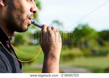 Close-up shot of bearded soccer referee blowing whistle after noticed infringement of game rules, blurred background