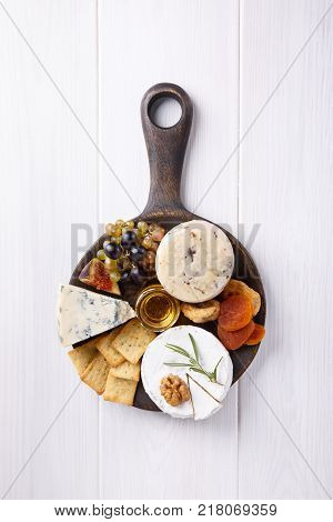 Cheese plate with blue cheese brie truffle hard cheese with grapes figs pears honey crackers dried fruits and nuts on white table. Top view. Copy space.