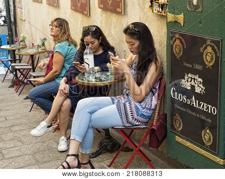 Ajaccio Corsica France: August 17 2017 Women sitting on the street watching their phones in the historic center of Ajaccio