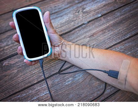 an arm with a cell phone hooked intravenously with the charger cord and a band aid covering the end tip - social media addiction concept 