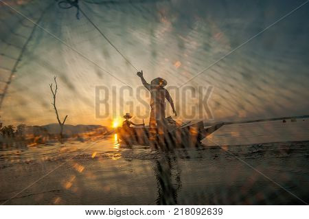Asian Fisherman On Wooden Boat Casting A Net For Catching Freshwater Fish In Nature River In The Ear