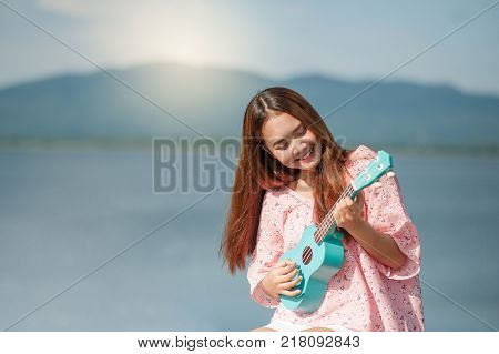 asian lady with hat play ukulele bossanova music in summer time.Young cute woman playing music outdo