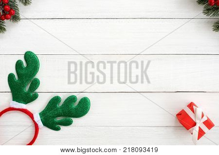 Christmas background. Christmas frame made of fir leaves holly berry christmas headband and red gift box on white wood background. Creative flat lay top view design