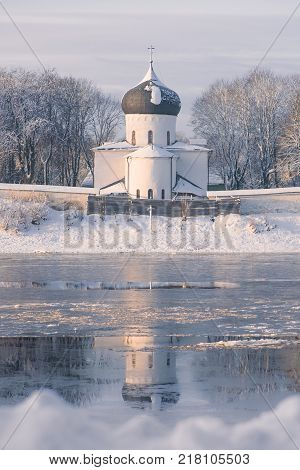 Vertical tonted purple shot of white stone Church reflected in the river. Winter landscape