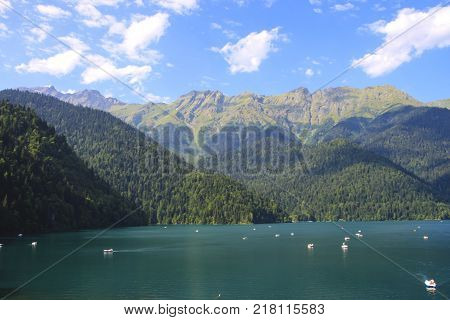 Beautiful panorama of natural mountain landscape. Pleasure boats on the water. Blue Lake Ritsa among mountains of the Caucasus, Abkhazia. Ritz Park