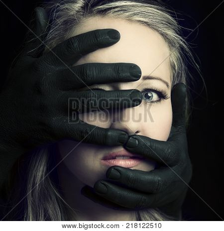 Frightened blonde woman grabbed by black hands on her face in artistic conversion