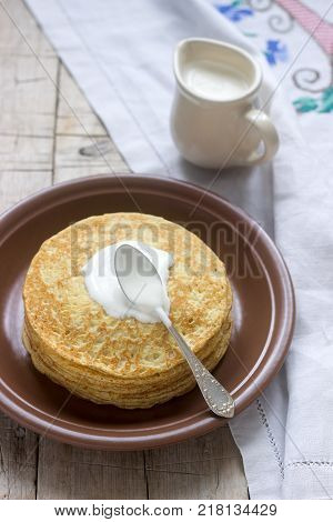 Stack of Russian pancakes with sour cream - blini on a plate on wooden table. Selective focus.