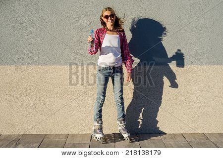 A beauty teen model girl, shod in rollerblades holding a water bottle. Sports, health and active leisure.