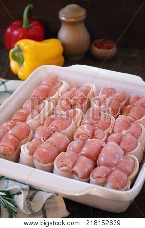 Raw meat paupiettes in ceramic bakeware and two bell peppers rustic style
