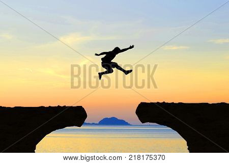 Man jump Mountain cliff sun light over silhouette