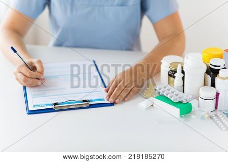 medicine, healthcare and people concept - nurse or doctor with drugs and clipboard writing prescription or medical report at hospital