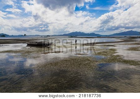 figures of girl and small ships in sibaltan beachin low tide time in El Nido, Phillipines, Palawan province with cloudly sky and mountain on foreground