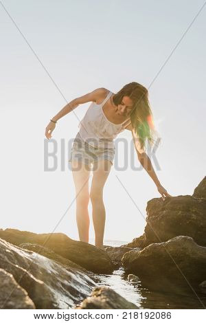 beautiful woman walk from water to the stone shore at dawn