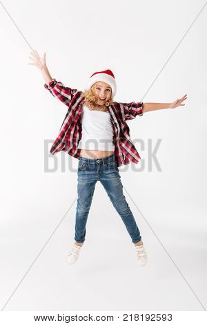 Full legth portrait of a cheery little girl dressed in christmas hat and looking at camera isolated over white background
