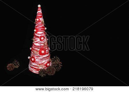Decorative bright Christmas tree handmade and cones on a black background. copy space.