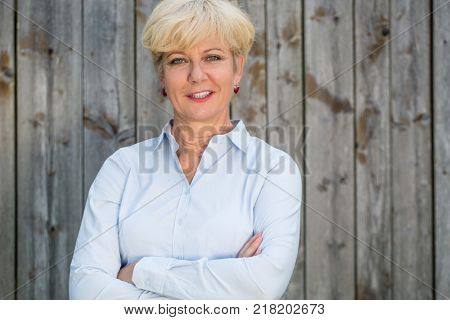 Portrait of a confident senior woman looking at camera while wearing a spotless shirt against a rustic wooden fence