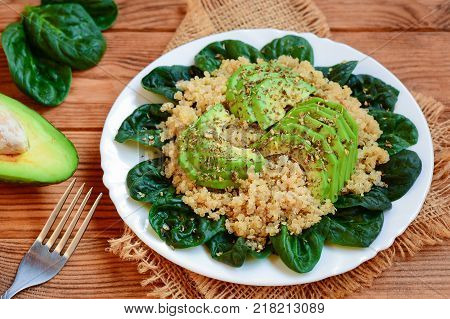 Avocado quinoa salad. Easy quinoa salad with fresh spinach leaves and avocado slices on a served plate. Brown wooden background. Rustic style. Closeup