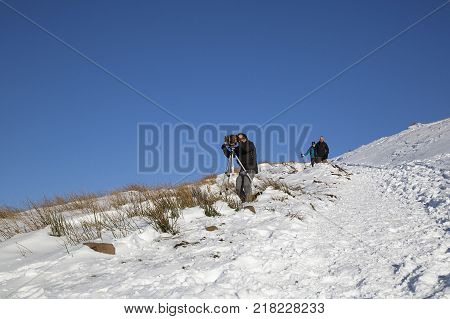 Pen y Fan, Wales, UK: December 11, 2017: A man takes a photograph with a vintage camera on the snow covered slopes of Pen y Fan mountain in the Brecon Beacons National Park with a winter blue sky background.