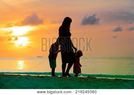 mother and two kids walking on tropical beach at sunset