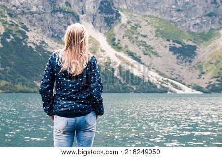 Blonde Girl stands back and looks at mountain lake